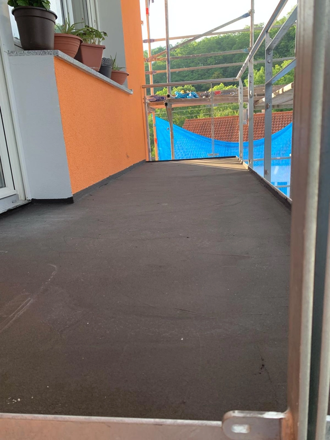 Bauabdichtungen- Bausanierungen Tiriakidis -  Komplette Renovierungsdienstleistungen – Blumentöpfe an orangefarbener Wand und frisch verlegter Betonboden